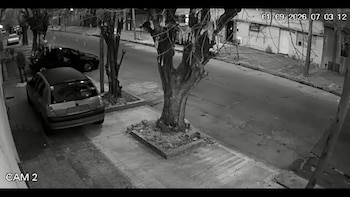 Captura en blanco y negro de una cámara de seguridad que muestra una calle residencial con automóviles estacionados y árboles