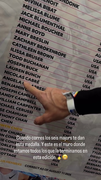 Una mano señala el nombre de Nicolás Cabré en un panel blanco impreso con una lista de nombres en letras mayúsculas negras