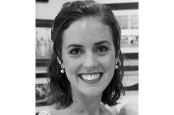 Retrato en primer plano y en blanco y negro de una mujer sonriente con pendientes de perlas y cuadros en la pared detrás de ella