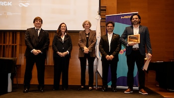 Cinco personas vestidas de traje posan de pie en un escenario junto a un cartel de Merck y una pantalla con el logotipo del CONICET
