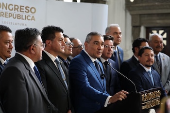Grupo de hombres en trajes formales, uno de ellos hablando desde un podio con micrófono. Al fondo, pared con el texto Congreso de la República