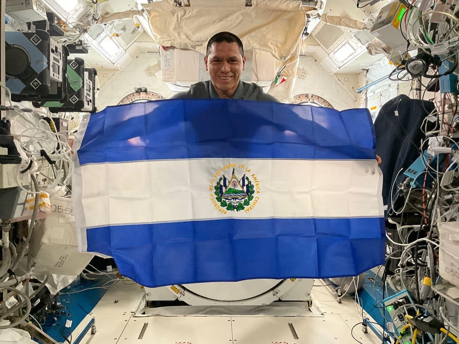 El astronauta estadounidense-salvadoreño Frank Rubio posa con la bandera de El Salvador a bordo de la Estación Espacial Internacional, celebrando su herencia mientras participa en pruebas para futuras misiones lunares de la NASA. (U.S. Embassy El Salvador)