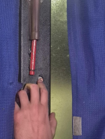 Mano humana, agujero en panel oscuro, cable rojo, tela azul y superficie metálica dorada