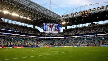 Vista interior del Hard Rock Stadium con miles de aficionados en las gradas verdes y azules, un campo de fútbol verde y una pantalla gigante