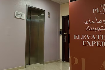 Pasillo interior con puerta de ascensor metálica, botón de llamada, cartel blanco con texto, puerta de madera, dispositivo de acceso y cartel promocional