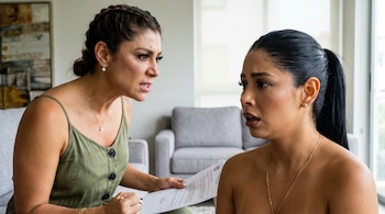 Karla Tarazona, en top verde con expresión furiosa, sostiene documentos frente a Pamela Franco, quien la mira sorprendida y preocupada en un interior.