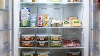 Estantes de un refrigerador con un cartón de leche, yogures, huevos, quesos, embutidos envasados y recipientes con comida etiquetada.