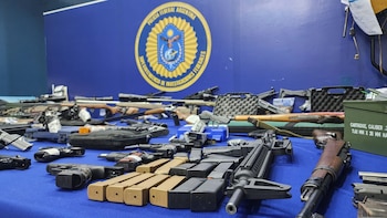 Una mesa azul cubierta con un gran número de armas de fuego, incluyendo pistolas, rifles, cargadores y cajas de municiones, con el escudo de la Policía Federal Argentina en el fondo