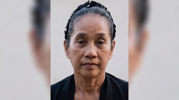 Primer plano del rostro de una mujer con el cabello recogido con una diadema negra y vestimenta oscura sobre un fondo liso.
