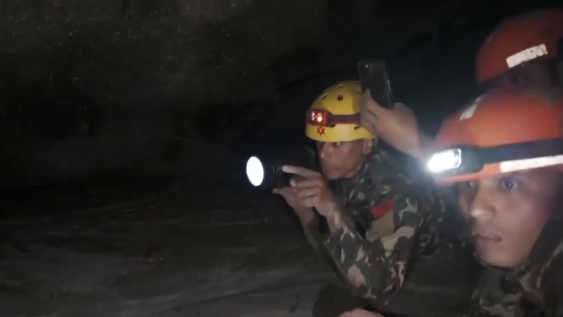 Equipos de rescate con linternas inspeccionan un espacio subterráneo a oscuras en Nepal para localizar personas con vida.