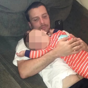 Hombre acostado en un sofá gris sosteniendo a un bebé que viste un pijama a rayas rojas y blancas, con la cabeza del bebé sobre el pecho del hombre