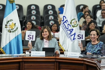 Dos mujeres sonrientes sostienen carteles de "SI" con el logo de SESAN en una mesa. Se ven las banderas de Guatemala y SESAN junto a ellas