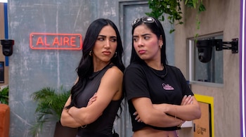 Dos mujeres, Mariana Zapata y Beba de la Cruz, de espaldas, con los brazos cruzados y expresiones serias, en un set con un letrero de neón 'AL AIRE'.