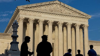 Siluetas de personas se alzan frente a la fachada columnada de la Corte Suprema de los Estados Unidos bajo un cielo azul claro
