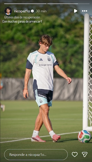 Nico Paz, futbolista, en ropa de entrenamiento de la selección argentina, caminando sobre el césped de un campo de fútbol con un balón a su lado