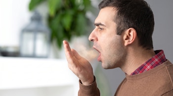Primer plano de un hombre exhalando visiblemente su aliento en la palma de su mano, con una expresión concentrada.