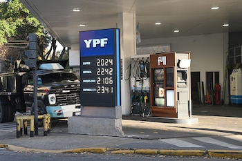 Un cartel de precios digital de YPF en una estación de servicio con los valores de nafta y diésel, un camión negro y surtidores de combustible