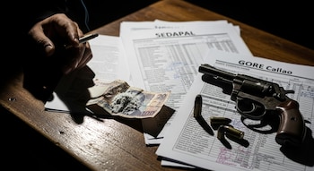 Una mano con cigarrillo encendido, un revólver, balas, billetes con polvo blanco y documentos de Sedapal y GORE Callao sobre una mesa de madera.