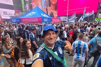 Hombre sonriente con camiseta y gorra de Argentina hace un pulgar arriba. Multitud de aficionados, banderas argentinas, pantallas gigantes y carpa azul