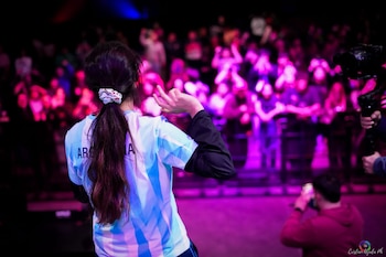 Vista trasera de una persona con camiseta de Argentina que gesticula hacia una multitud iluminada con luces violetas
