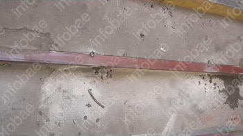 Primer plano de un escalón de concreto gris deteriorado con una barra metálica horizontal de color rojo y algunos escombros sueltos