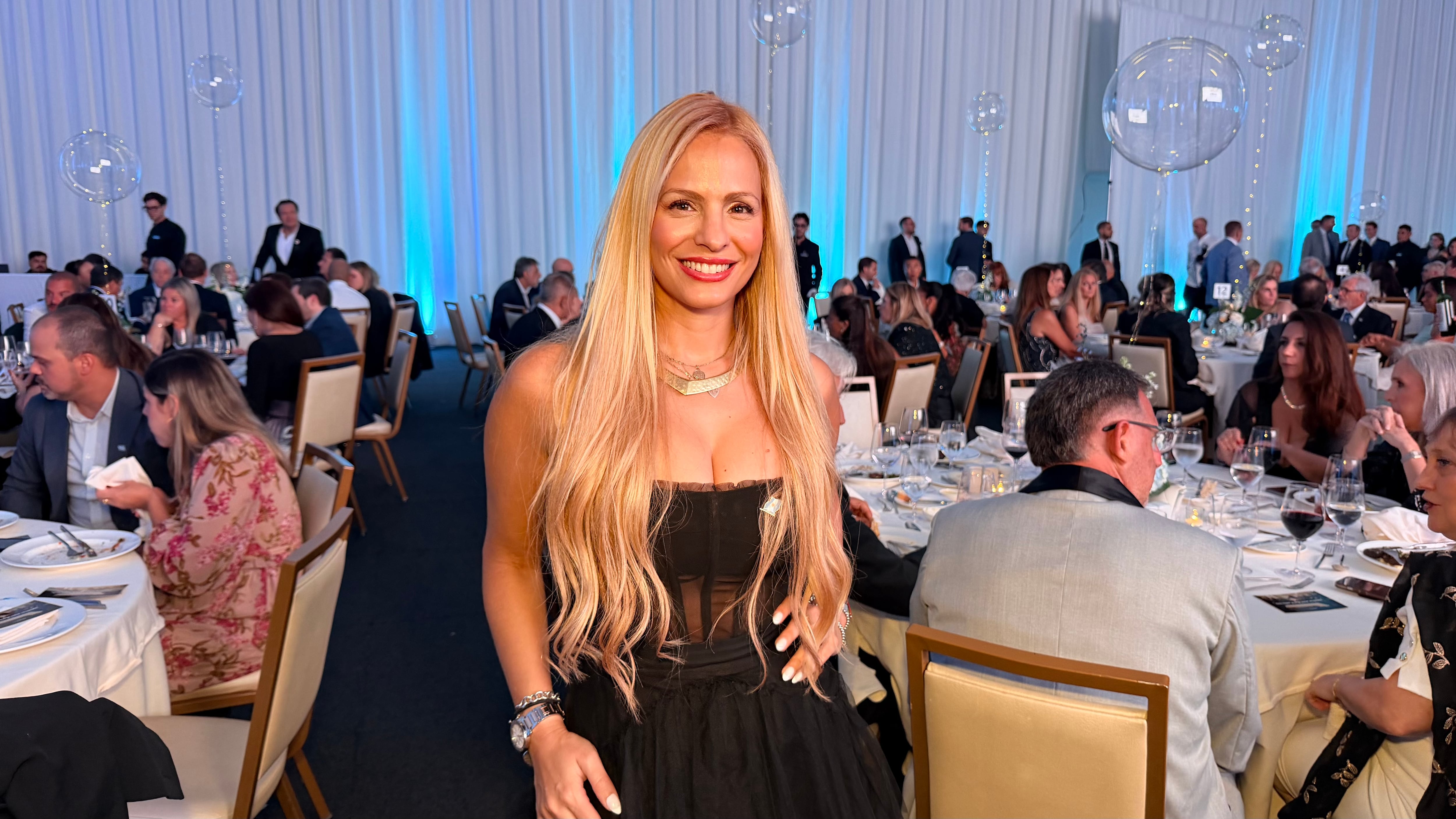 Antonella Fredianelli posa sonriente en la gala anual de La Cámara Argentino-Americana de Comercio en Miami, rodeada de invitados en una noche de celebración empresarial.