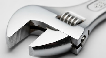 Una llave inglesa ajustable de metal, con mordazas lisas, un tornillo sin fin y acabados metálicos brillantes sobre un fondo claro y desenfocado.