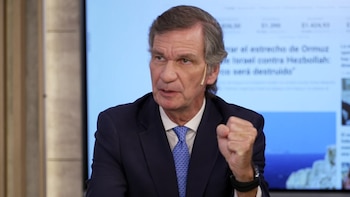 Un hombre de mediana edad con cabello gris, traje azul y corbata, habla con seriedad y el puño derecho cerrado, con un auricular en su oreja