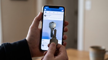 Dos manos sostienen un teléfono inteligente que muestra una publicación de red social con una imagen de llave, y una llave metálica oxidada.