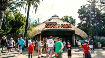 Entrada techada de paja al San Diego Zoo Safari Park con el nombre visible, palmeras y una multitud de personas caminando