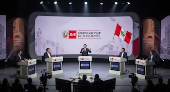 Escenario de debate político en Perú con cinco candidatos. Un orador central y cuatro sentados. Pantalla con logo JNE, bandera peruana. Público y cámaras en primer plano.