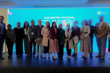 Seis mujeres sentadas en un escenario frente a una pantalla azul con la inscripción Encuentro Nacional PLANEA