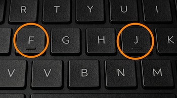 Primer plano de un teclado de laptop negro. Las teclas F y J, con su relieve táctil, están encerradas en círculos naranja brillantes.