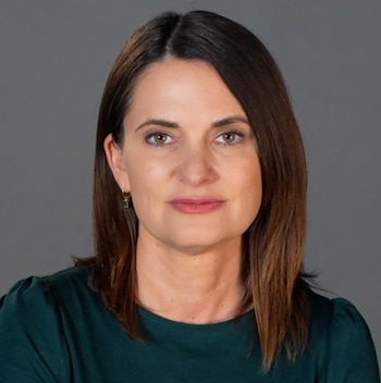 Retrato de frente de una mujer con cabello castaño hasta los hombros y ropa verde oscuro sobre un fondo gris