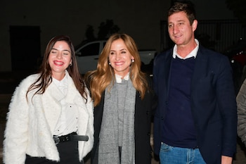 Tres personas, dos mujeres y un hombre, posan sonriendo. El hombre viste blazer azul y jeans. Una mujer lleva saco blanco. Otra mujer viste abrigo oscuro y bufanda gris