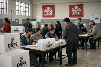 Interior de un centro de votación en Perú con varias mesas y cabinas de votación blancas de la ONPE, personas sentadas y de pie, y logos del JNE en pancartas.