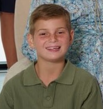 Retrato de un niño sonriente con cabello rubio corto, pecas y una camisa polo verde