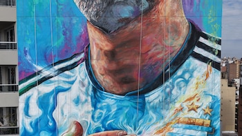 Primer plano de un mural en un edificio que representa el cuello y parte del rostro de Lionel Messi, con camiseta argentina, tres estrellas doradas y fondo multicolor