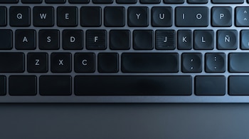 Vista cenital de un teclado de computadora negro con letras blancas. Se observan las teclas A, S, D, F, J, K, L, Ñ, con las teclas F y J mostrando rayas táctiles en relieve.