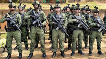 Un grupo de soldados del GOER con uniformes verdes, cascos, gafas de sol y chalecos tácticos, sostienen rifles en posición de firmes en un entorno exterior.