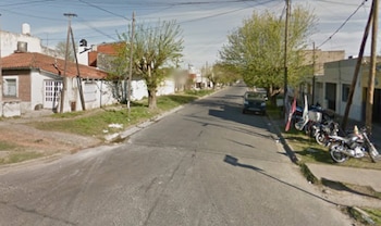 Una calle residencial con casas de un piso, árboles, un coche y varias motocicletas estacionadas al borde. El cielo es parcialmente azul con algunas nubes