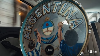 Primer plano de tambor con ilustración de palabra Argentina, escudo nacional, dos figuras levantando una cinta. Logotipo de Uber visible. Dentro de un vehículo