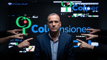 Plano medio de un hombre en traje y camisa a cuadros, rodeado de manos que lo señalan, con el logotipo de Colpensiones al fondo.