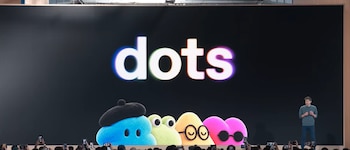 Una pantalla con la palabra dots y personajes coloridos junto a un hombre en un escenario frente al público