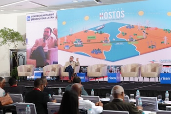 Un hombre habla en un escenario frente a una pantalla con un diagrama del Proyecto Hostos, que muestra una interconexión energética submarina entre dos islas. Hay una audiencia
