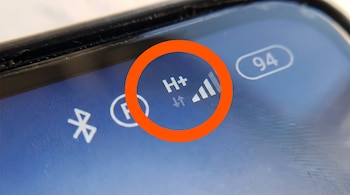 Primer plano de pantalla de celular con el icono H+ de red móvil, un círculo naranja, barras de señal, el número 94 de batería y el símbolo de Bluetooth.