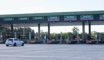 Estación de peaje con varias cabinas, carteles de Telepase y pago electrónico, luces verdes y un automóvil blanco a la izquierda