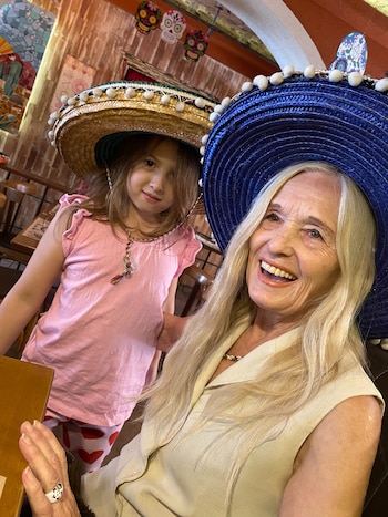 Una mujer con sombrero azul sonríe junto a una niña con sombrero de paja en un restaurante con adornos de calaveras mexicanas