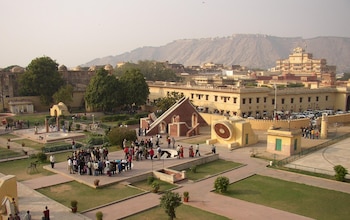 Vista aérea de Jantar Mantar con instrumentos astronómicos de piedra y personas. Al fondo, el Palacio de la Ciudad y una montaña árida
