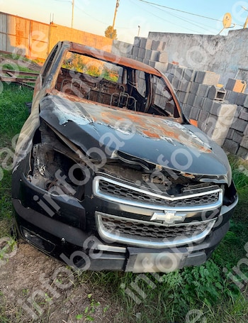 Parte frontal de un vehículo Chevrolet quemado y sin vidrios, ubicado sobre césped cerca de una pila de bloques de concreto